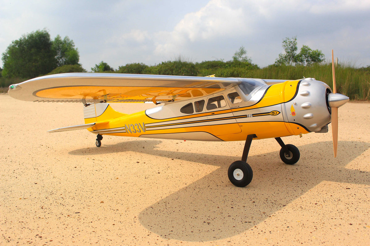 Yellow and gray model airplane on a sandy surface with trees in the background